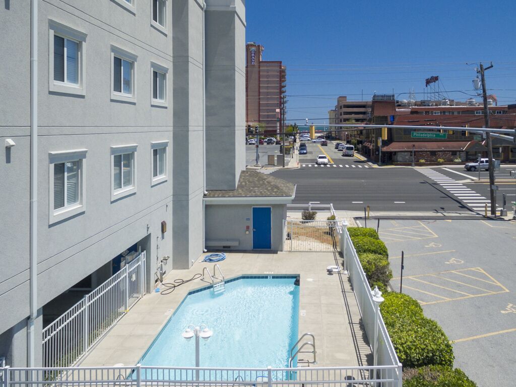 Un immeuble avec une piscine, un parking et une rue où circulent des voitures.