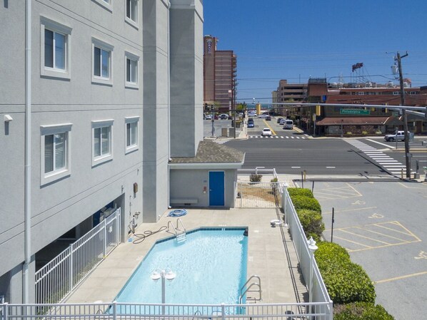 A building with a swimming pool, a parking lot, and a street with cars. - Luxurious three bedroom condo. Enjoy stunning views from inside the unit. (Ocean City)