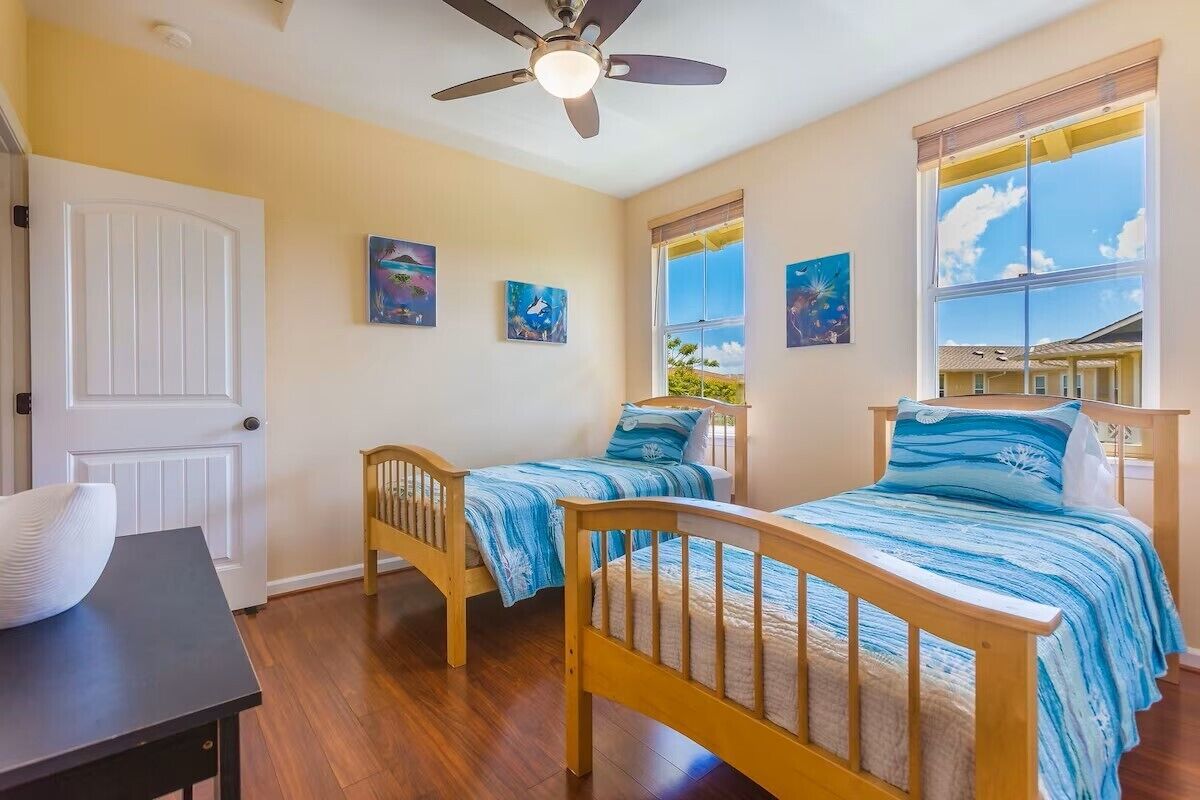 A bedroom with two wooden beds, a ceiling fan, and a window with a view of a house.