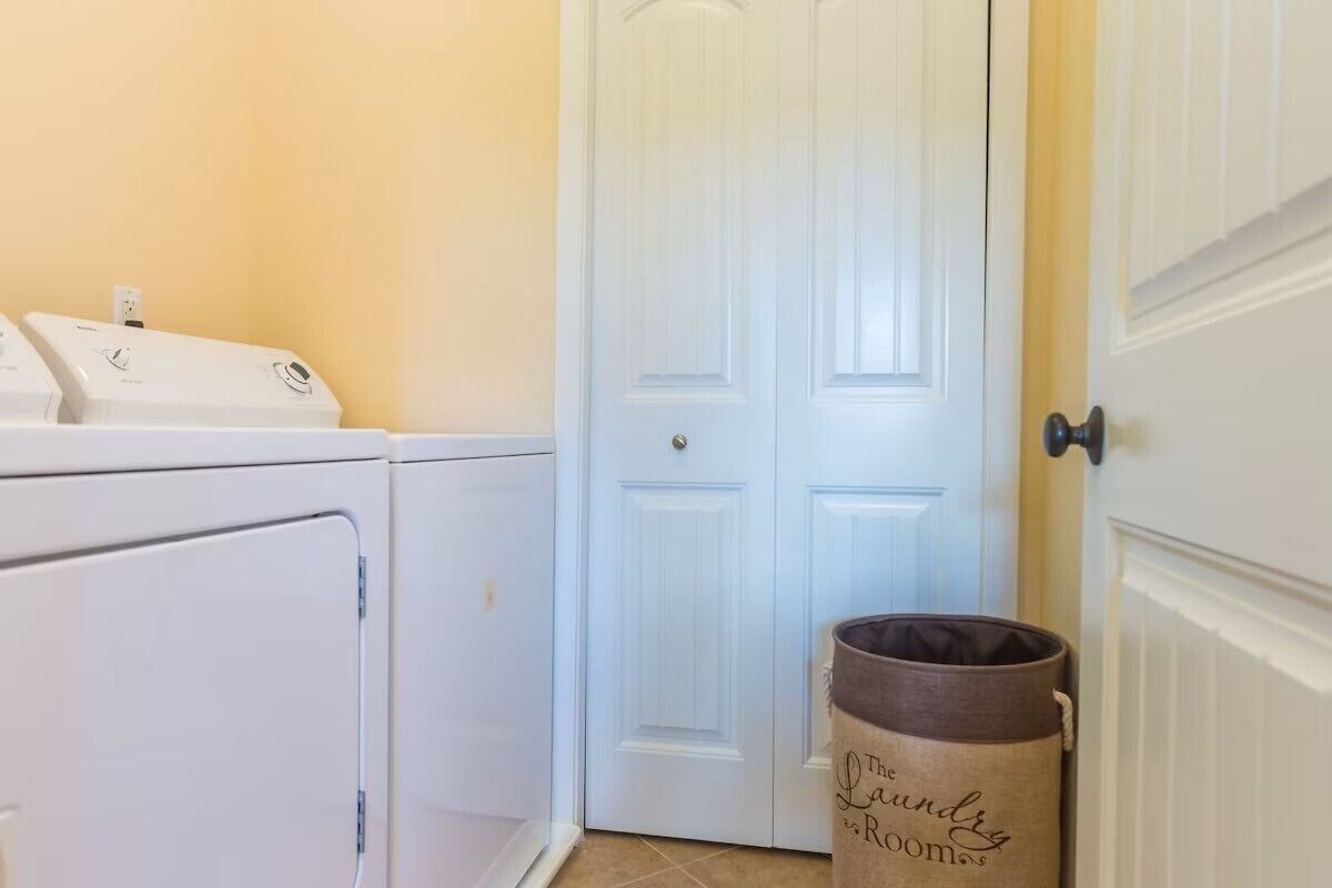 A laundry room with a washing machine, dryer, and a trash can labeled "The Laundry Room."