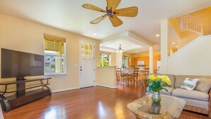 A spacious living room with hardwood flooring, a flat-screen TV, a ceiling fan, a dining area with a chandelier, and a staircase leading to another level. - Amazing private home with AC, Pool, Garage, Hot Tub and Toys N27C (Princeville)