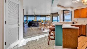 A spacious living area with a large window overlooking the ocean, a dining area with wicker furniture, and a kitchen with wooden cabinets. - *Fall into Savings-20% Off New Bookings thru 2026* (Garden City)