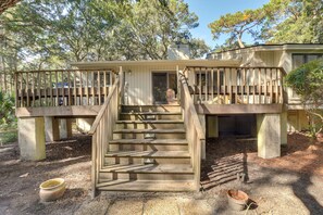 Eine Holzterrasse mit einer Treppe zu einem überdachten Bereich, umgeben von Bäumen.