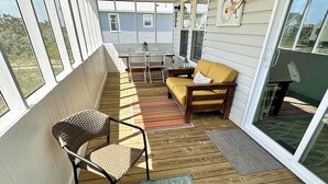 A covered outdoor patio with a wooden deck, wicker chairs, a glass table, and a sofa.
