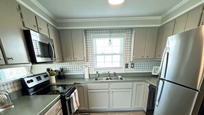 A modern kitchen with light wood flooring, stainless steel appliances, and a window with a view.
