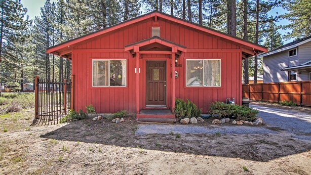 Una casa roja de un piso con porche, un pequeño jardín y valla de madera.