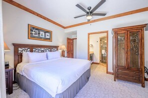 A bedroom with a large bed, a ceiling fan, a wooden cabinet, and a framed picture on the wall.