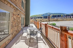 Ein Balkon mit Sitzgelegenheit im Freien, ein Steinhaus und Blick auf einen Parkplatz sowie Hügel.