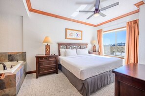 A hotel room with a bed, a nightstand, a lamp, a window with curtains, and a view of the outside. - Westgate 4408 (Park City)