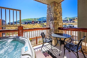 A hot tub on a balcony with a stone pillar, two chairs, and a view of a parking lot and hills. - Westgate 4408 (Park City)