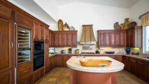 A kitchen with wooden cabinets, a central island, and a large window. - Ocean View 5 BR Luxury Villa Las Brisas Includes Private Pool, Jacuzzi & Wet Bar (San Jose del Cabo)