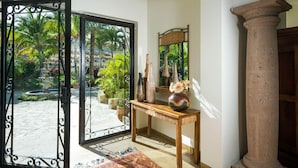 A room with a large glass door leading to a garden, a wooden console table with vases, and a mirror on the wall. - Ocean View 5 BR Luxury Villa Las Brisas Includes Private Pool, Jacuzzi & Wet Bar (San Jose del Cabo)