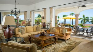 A spacious living room with a large window, a chandelier, and a view of the ocean. - Ocean View 5 BR Luxury Villa Las Brisas Includes Private Pool, Jacuzzi & Wet Bar (San Jose del Cabo)