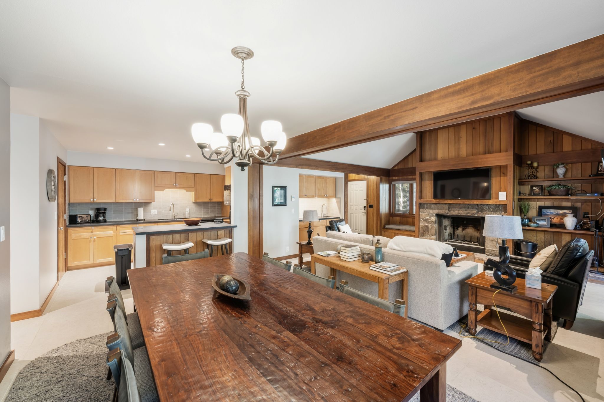 Een ruime woonkamer met een houten eettafel, een open haard en een keuken met houten kastjes.
