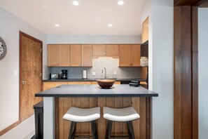 A kitchen with wooden cabinets, a large island with stools, a coffee maker, and a sink. - Teewinot D5: Teton Village- Beautiful- Top Floor- Sleeps 10- Pool Access (Teton Village)