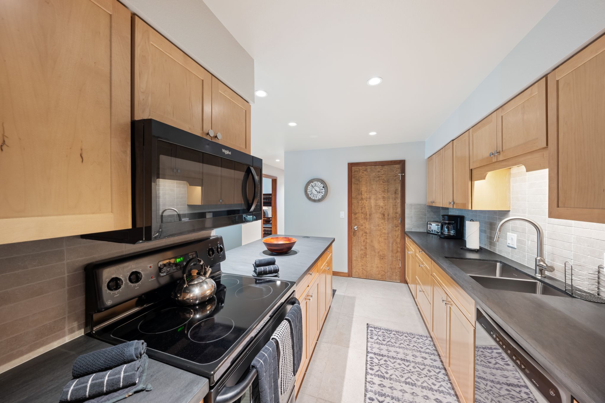 Una cocina moderna con armarios de madera, microondas negro, estufa y cafetera.