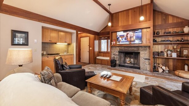 A cozy living room with a fireplace, a television, and a kitchen area in the background.
