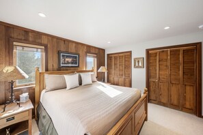 A bedroom with a large bed, wooden panel walls, a window, and a wardrobe. - Teewinot D5: Teton Village- Beautiful- Top Floor- Sleeps 10- Pool Access (Teton Village)