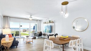 Een ruime woonkamer met een eettafel, stoelen, een bank, een televisie en uitzicht op de omgeving.