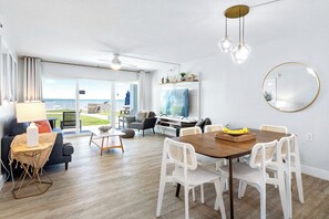 A modern living room with a dining area, large windows, and a view of the outdoors. - Beachfront Comfort: Ground-Floor Unit with Stunning Views, Heated Pool & BBQ Grill! (Satellite Beach)