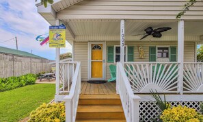 A wooden house with a porch, a yellow door, and a sign for 'Vacation Here!'