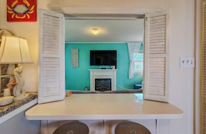 A room with a teal wall, a fireplace, a television, and a table with a lamp.