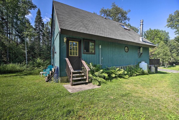 A green wooden cabin with a chimney, a front door, and a small porch with steps.