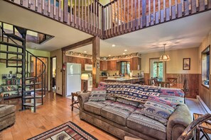 A spacious living area with a large sofa, a wooden staircase, and a kitchen in the background.