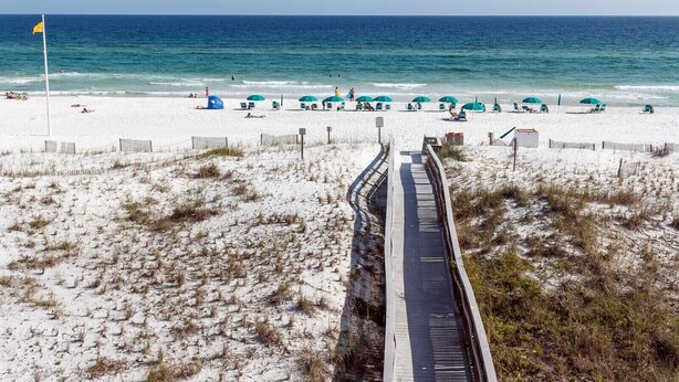 Ein Strand mit einer Holzpromenade, die zum Wasser führt, feinem Sand und Strandsonnenschirmen.