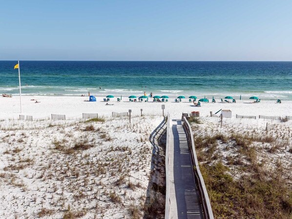 Een strand met een houten boardwalk die naar het water leidt, zandstrand en strandparasols.