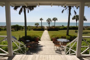A covered outdoor area with a wooden deck, two round tables with chairs, and a view of the ocean.