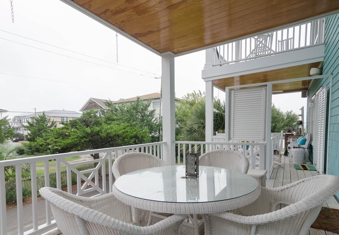 A covered outdoor area with a round glass table and wicker chairs.