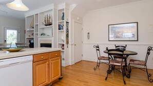 A kitchen with wooden cabinets, a white dishwasher, and a dining area with a round table and four chairs. - Charming 3 BR townhouse with sound views! (Wrightsville Beach)