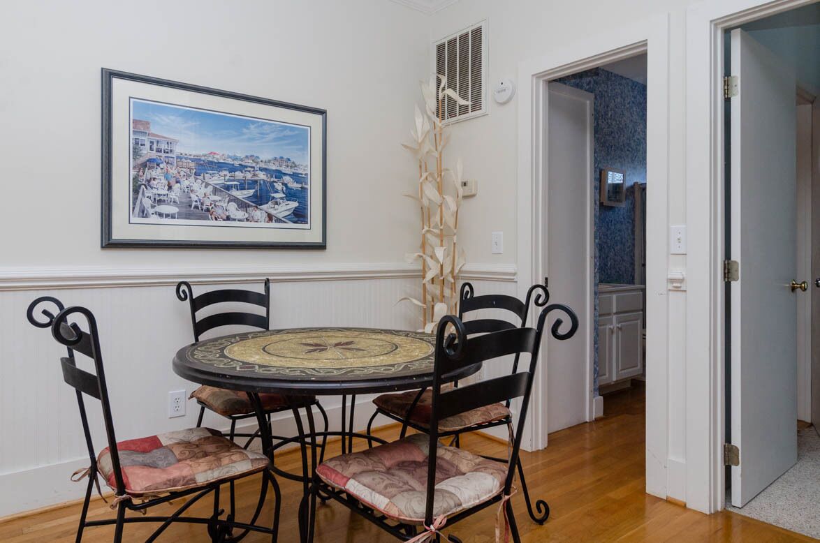 Un comedor con una mesa redonda y cuatro sillas, un cuadro enmarcado en la pared y una puerta que da a otra habitación.
