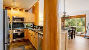 A modern kitchen with wooden cabinets, stainless steel appliances, and a large window offering a view of the outdoors. - Spacious 3.5BR Retreat | Golf Course Views | Walk to Lakes & Trails | Managed By Aloha Whistler (Whistler)