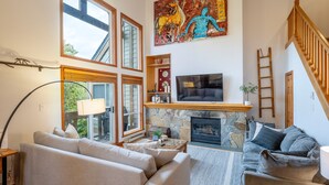 A living room with a stone fireplace, a television, and a painting. - Spacious 3.5BR Retreat | Golf Course Views | Walk to Lakes & Trails | Managed By Aloha Whistler (Whistler)