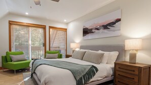 A modern bedroom with a large bed, a green armchair, a wooden nightstand, and a painting on the wall. - Spacious 3.5BR Retreat | Golf Course Views | Walk to Lakes & Trails | Managed By Aloha Whistler (Whistler)