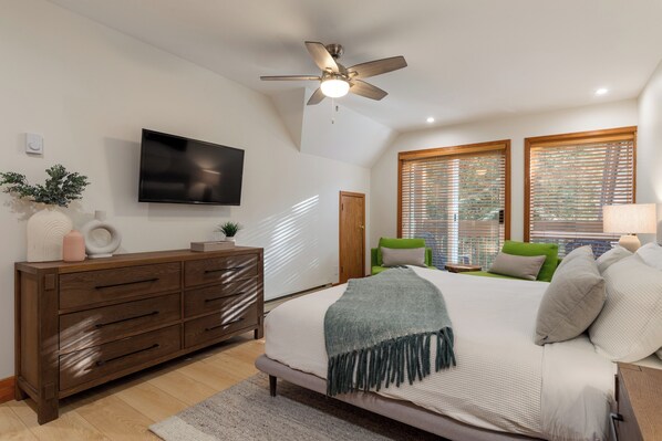 A bedroom with a bed, a ceiling fan, a TV, a dresser, and a window with blinds.