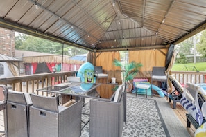 Une terrasse extérieure aménagée avec des meubles en osier, une table et un espace couvert offrant une vue sur le jardin arrière.