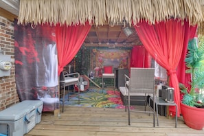 Un espace extérieur accueillant, aménagé avec des meubles en osier, des rideaux rouges et un toit de chaume.