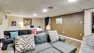 A living room with a grey sectional sofa, a bed, a desk, and a painting on the wall.