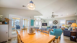 A spacious living room with a wooden dining table, comfortable seating, a television, and nautical decor. - Bali Hai - Kitty Hawk MP 3, 50 Yards to Beach, Breathtaking Views, Open Decks (Kitty Hawk)