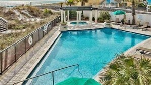Une piscine rectangulaire, bordée d’une terrasse carrelée, entourée de chaises longues et de parasols.