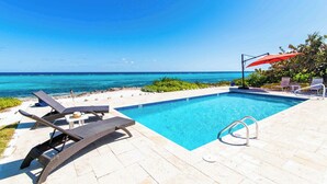 A pool with lounge chairs and umbrellas, overlooking a beach and ocean. - Thatch Hill: Beach House w/ Private Pool & Backyard Snorkeling, Walk to the Rum Point Club! (Grand Cayman)