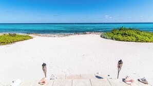 A beach with a clear view of the ocean, a sandy path leading to the water, and some greenery on the sides. - Thatch Hill: Beach House w/ Private Pool & Backyard Snorkeling, Walk to the Rum Point Club! (Grand Cayman)