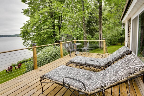 Une terrasse en bois avec deux chaises longues et une table, d’où l’on a vue sur un lac et qui est entourée d’arbres.
