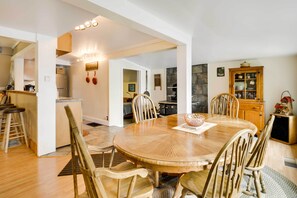 Un coin repas avec une table et des chaises en bois, une cuisine en arrière-plan et un meuble avec des portes en verre.