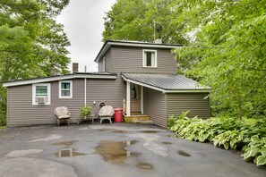 Une maison à deux étages avec un porche couvert, un petit garage attenant et une allée menant à la maison, où l’on voit des flaques d’eau.