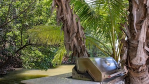 Une plateforme en pierre sur laquelle se trouve un objet métallique, qui pourrait être un gril, dans un environnement luxuriant et verdoyant, avec des arbres et une étendue d’eau.