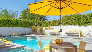 Ein Poolbereich mit Liegestühlen, einem Tisch und Stühlen sowie einem gelben Sonnenschirm.